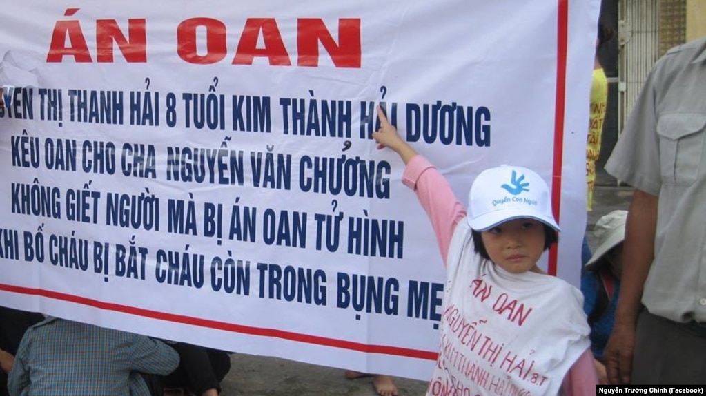 Con gái của tử tù Nguyễn Văn Chưởng mặc áo và đứng trước băng rôn kêu oan cho bố của mình bị kết án tử hình vì cáo buộc "giết người", một bản án đang bị hàng nghìn người trong nước và cộng đồng quốc tế phản đối.