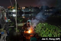 Nguyen Thi Thuy lights a fire on her boat while getting ready for her day's work in Can Tho, Vietnam, Wednesday, Jan. 17, 2024. (AP Photo/Jae C. Hong)