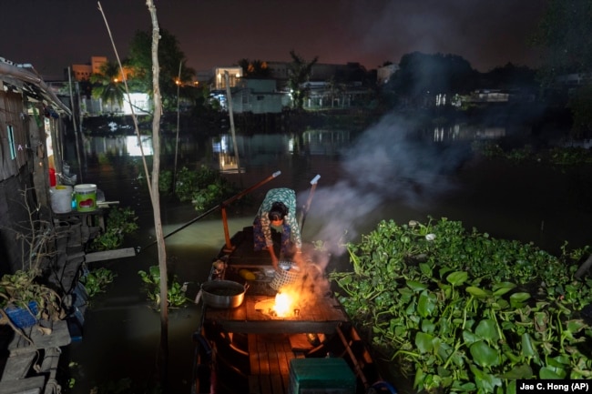 Nguyen Thi Thuy lights a fire on her boat while getting ready for her day's work in Can Tho, Vietnam, Wednesday, Jan. 17, 2024. (AP Photo/Jae C. Hong)