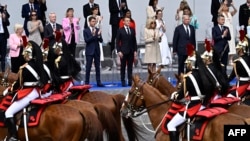 France's Prime Minister Gabriel Attal, President Emmanuel Macron and first lady Brigitte Macron applaud as the Cavalry Regiment of the French Republican Guard rides past during the Bastille Day military parade in Paris, July 14, 2024. 