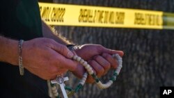 Seorang warga tampak berdoa dengan rosario di lokasi pembunuhan Uskup David O’Connell di Hacienda Heights, California, pada 19 Februari 2023. (Foto: AP/Damian Dovarganes)