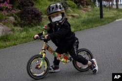 FILE - Seorang anak yang mengenakan masker dan helm, mendorong sepeda mininya di East Lake Park, Wuhan, provinsi Hubei, China tengah, 2 April 2020. (Ng Han Guan/AP)