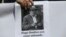 FILE - A protester holds a photo of journalist Hugo Bustios, outside a court during the trial of Peru's former military intelligence chief Daniel Urresti for his alleged role in Bustios' 1988 murder, in Lima, Peru, Oct. 4, 2018. The sign reads "Hugo Bustios is still watching."
