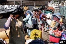 Migran asing membawa barang-barang mereka saat diusir oleh petugas Kepolisian Afrika Selatan (SAPS) dari tempat tinggal sementara yang dibangun di depan kantor Komisaris Tinggi PBB untuk Pengungsi (UNHCR) di Pretoria, 21 April 2023. (Phill Magakoe / AFP)