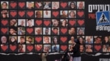 FILE - A woman and her children walk past a wall with photographs of hostages who were kidnapped during the Oct. 7, 2023, Hamas cross-border attack in Israel, on Feb. 26, 2024, in Jerusalem.