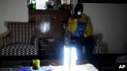 A Kenyan sips a cup of tea as she sits in her sitting room with an emergency light amid a power outage Aug. 26 2023. 