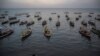 Orang-orang duduk di samping perahu tradisional di sepanjang garis pantai di Surabaya, Jawa Timur.