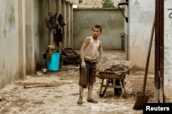 A boy looks on while standing next to a wheelbarrow, in the aftermath of floods following heavy rain, in Sheikh Jalal District, Baghlan province, Afghanistan, May 11, 2024.