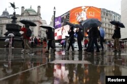 Para pejalan kaki melewati Piccadilly Circus di London, Inggris, sambil memegang payung, 9 Juli 2024. (REUTERS/Hollie Adams)