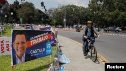 A person rides a bicycle next to posters of candidates for the general elections, in Guatemala City, Guatemala, March 27, 2023.