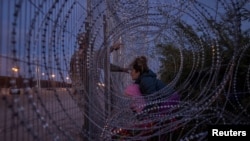 Seorang migran tambak membawa bayinya saat ia bersitegang dengan tentara nasional AS di antara kawat besi yang terpasang di wilayah perbatasan di El Paso, Texas, pada 26 Maret 2024. (Foto: Reuters/Adrees Latif)