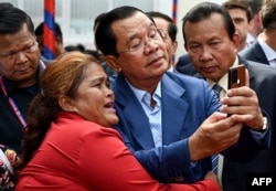 FILE - Cambodia's Prime Minister Hun Sen (C) takes selfies with a supporter during the inauguration ceremony of the Bakheng-1 water treatment plant in Phnom Penh on June 19, 2023.