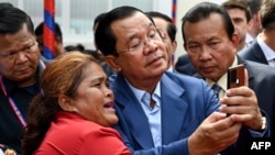 Cambodia's Prime Minister Hun Sen (C) takes selfies with a supporter during the inauguration ceremony of the Bakheng-1 water treatment plant in Phnom Penh on June 19, 2023. (Photo by TANG CHHIN Sothy / AFP)