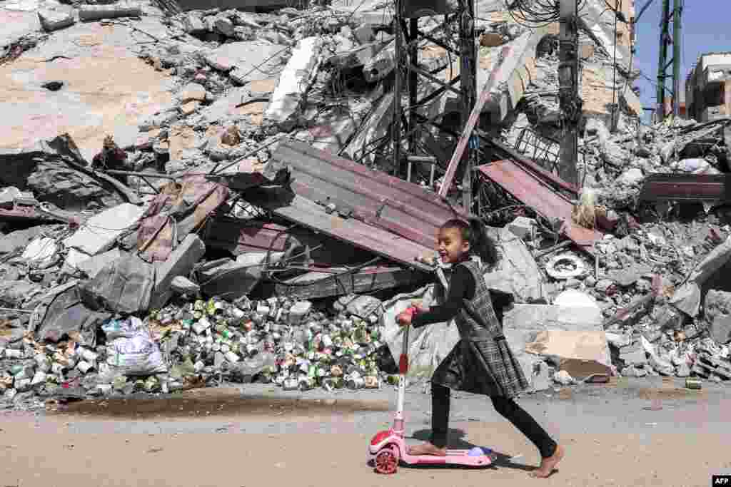 A girl rides a scooter past the rubble of a destroyed building in Rafah in the southern Gaza Strip, amid the ongoing conflict in the Palestinian territory between Israel and the militant group Hamas.