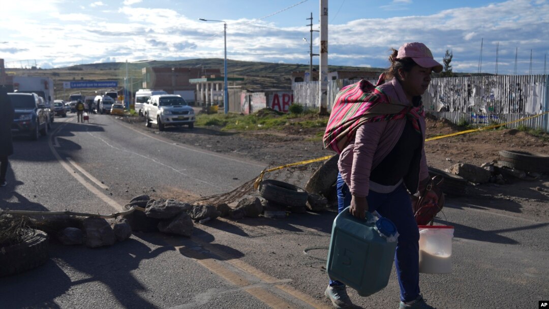 Una mujer cargada con contenedores llenos de leche atraviesa caminando los bloqueos de carretera colocados por los manifestantes de oposición al gobierno en la carretera de Juliaca, sur de Perú, a Puno, Bolivia, el viernes 10 de marzo de 2023.