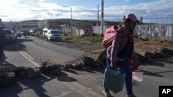 Una mujer cargada con contenedores llenos de leche atraviesa caminando los bloqueos de carretera colocados por los manifestantes de oposición al gobierno en la carretera de Juliaca, sur de Perú, a Puno, Bolivia, el viernes 10 de marzo de 2023.