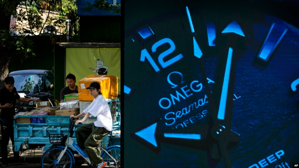 A woman rides past delivery workers sorting parcels near an advertisement for luxury watches in Beijing, Sept. 20, 2023