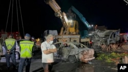 Turkish police officers and emergency personnel work next to burned vehicles after a crash on the Iskenderun-Antakya highway, south Turkey, late Saturday, May 6, 2023. 