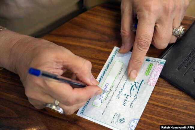 Seorang perempuan Iran sedang menyiapkan surat suara di sebuah tempat pemungutan suara (TPS) di Teheran dalam pemilihan presiden, Jumat, 28 Juni 2024. (Foto: Raheb Homavandi/AFP)