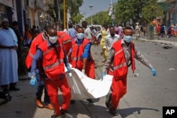 FILE - Medics carry away the dead body of a woman killed after a blast outside a restaurant in Mogadishu, Somalia, March 28, 2019.
