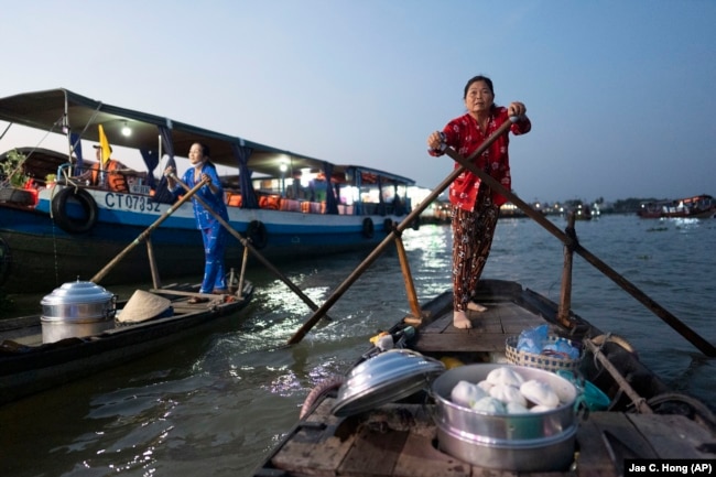 Nguyen Thi Thuy quickly rows to a passing tourist boat in the floating market of Can Tho, Vietnam, Jan. 17, 2024. (AP Photo/Jae C. Hong)