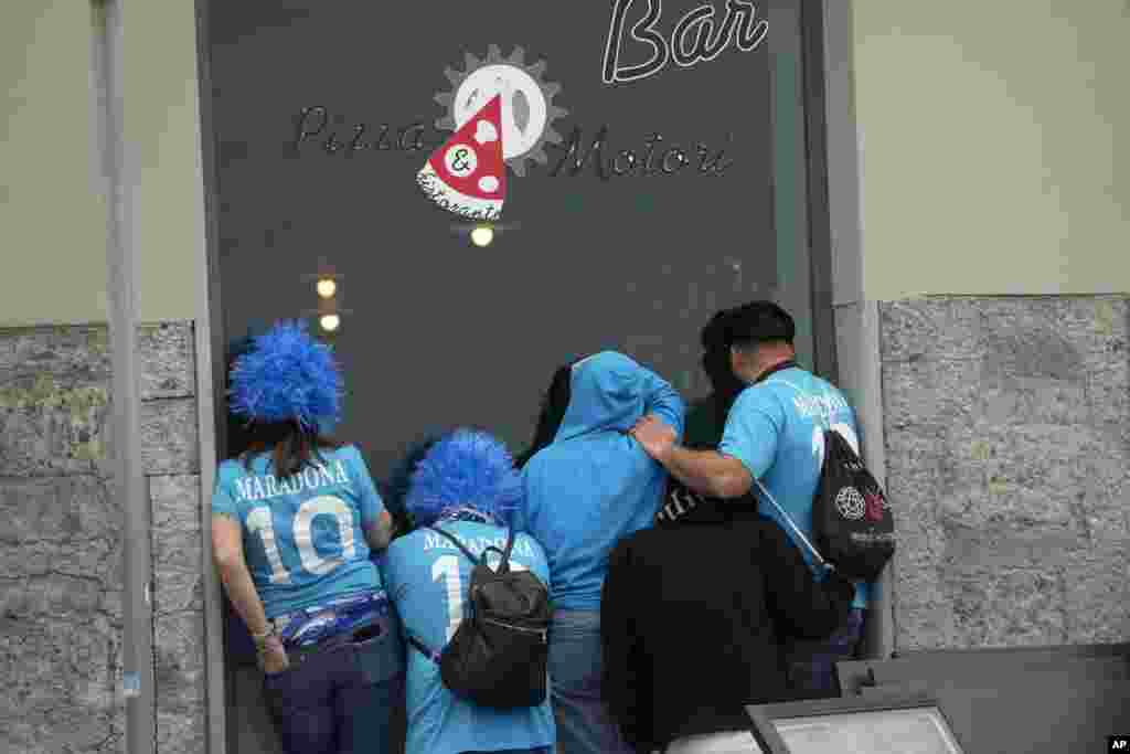 Napoli fans lean against the window of a Pizza restaurant to watch the Serie A soccer match between Napoli and Salernitana being played at the Diego Armando Maradona stadium, in Naples, Italy.