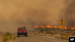 A car passes rising flames from the York Fire in the Mojave National Preserve, California, July 30, 2023.