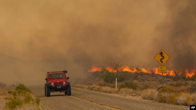 A car passes rising flames from the York Fire in the Mojave National Preserve, California, July 30, 2023.