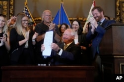 FILE - Minnesota Governor Tim Walz, middle, holds a bill he signed to legalize recreational marijuana for people over the age of 21, May 30, 2023.