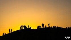 Palestinians are silhouetted against the setting sun as they stand on a hill on the Gaza-Egypt border in Rafah, on the southern Gaza Strip, on Dec.r 26, 2023.