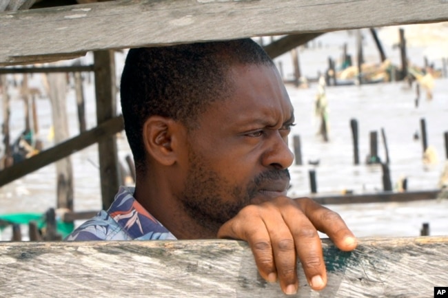 Stephen Tunlese, who lost his house and shop due to coastal erosion, stands inside damaged stilt house looking at the sea in Ayetoro, Southwest Nigeria, Friday, April 5, 2024. (AP Photo/Dan Ikpoyi)