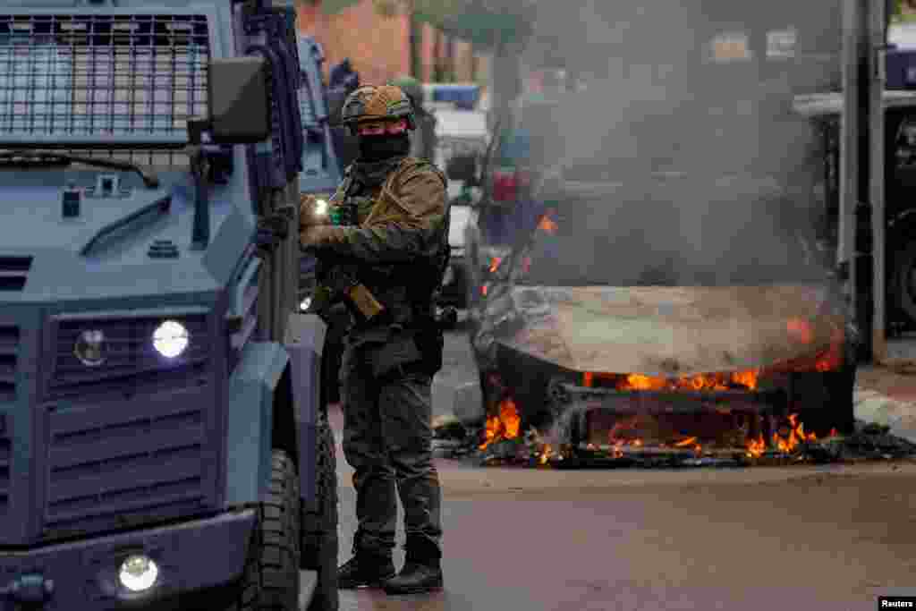 A special police forces officer stands next to a burning car, following clashes between Kosovo police and ethnic Serb protesters, who tried to prevent a newly-elected ethnic Albanian mayor from entering his office, in the town of Zvecan, Kosovo.