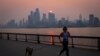 Una mujer trota con un perro a lo largo del río Hudson poco después del amanecer, mientras la neblina y el humo causados ​​por los incendios forestales en Canadá se ciernen sobre el horizonte de Manhattan, en la ciudad de Nueva York, Nueva York, EEUU, 7 de junio de 2023.