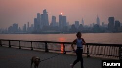 Una mujer trota con un perro a lo largo del río Hudson poco después del amanecer, mientras la neblina y el humo causados ​​por los incendios forestales en Canadá se ciernen sobre el horizonte de Manhattan, en la ciudad de Nueva York, Nueva York, EEUU, 7 de junio de 2023.