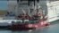 This image from video shows a ship belonging to Spanish aid group Open Arms, background, and a barge docked at Larnaca port in Cyprus, March 11, 2024. World Central Kitchen posted on X that the ship, loaded with some 200 tons of food, set sail on March 12.
