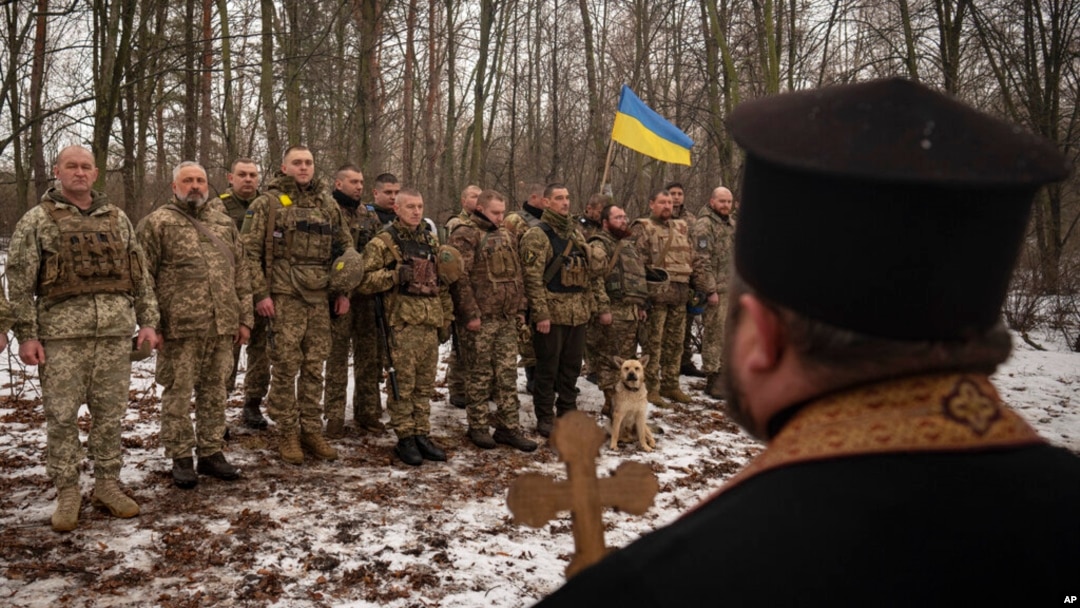 Священник благословляет украинских солдат во время церемонии поднятия флага, в Харьковской области, Украина, 25 февраля 2023 года.