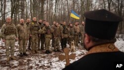 Священник благословляет украинских солдат во время церемонии поднятия флага, в Харьковской области, Украина, 25 февраля 2023 года.