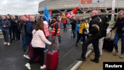 FILE: Passengers walk on the road with their luggage as airport workers on strike gather during the ninth day of nationwide strikes and protests against French government's pension reform, at the Paris-Charles de Gaulle airport near Paris, France, March 23, 2023. 