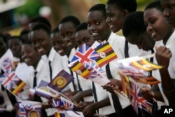 FILE - Ugandan children wave flags to receive Britain's Prince Charles at St. Joseph's School in Naggalama,on the outskirts of Kampala, Uganda, Nov. 24, 2007.