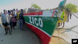 In this video grab, people stand next to a boat that local media say capsized the day before off Mozambique's Nampula province, April 8, 2024. (Television Mozambique via AP)