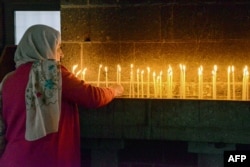 FILE - A woman lights candles during the Easter mass at the Armenian church Surp Giragos, in Diyarbakir, southeastern Turkey, on April 9, 2023. This week on Ask a Teacher, we will answer a question about different kinds of religious centers. (Photo by Seyfettin GUNCEL / AFP)