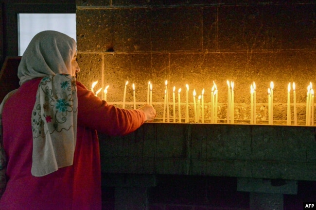 FILE - A woman lights candles during the Easter mass at the Armenian church Surp Giragos, in Diyarbakir, southeastern Turkey, on April 9, 2023. This week on Ask a Teacher, we will answer a question about different kinds of religious centers. (Photo by Seyfettin GUNCEL / AFP)