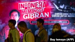 Para pendukung Gibran Rakabuming Raka, putra sulung Presiden Joko Widodo, berjalan di depan poster di Jakarta ajakan untuk mendukung pencalonan Gibran sebagai bakal calon wakil presiden dalam pemilihan presiden 2024, Sabtu, 21 Oktober 2023. (Foto: Bay Ismoyo/AFP)