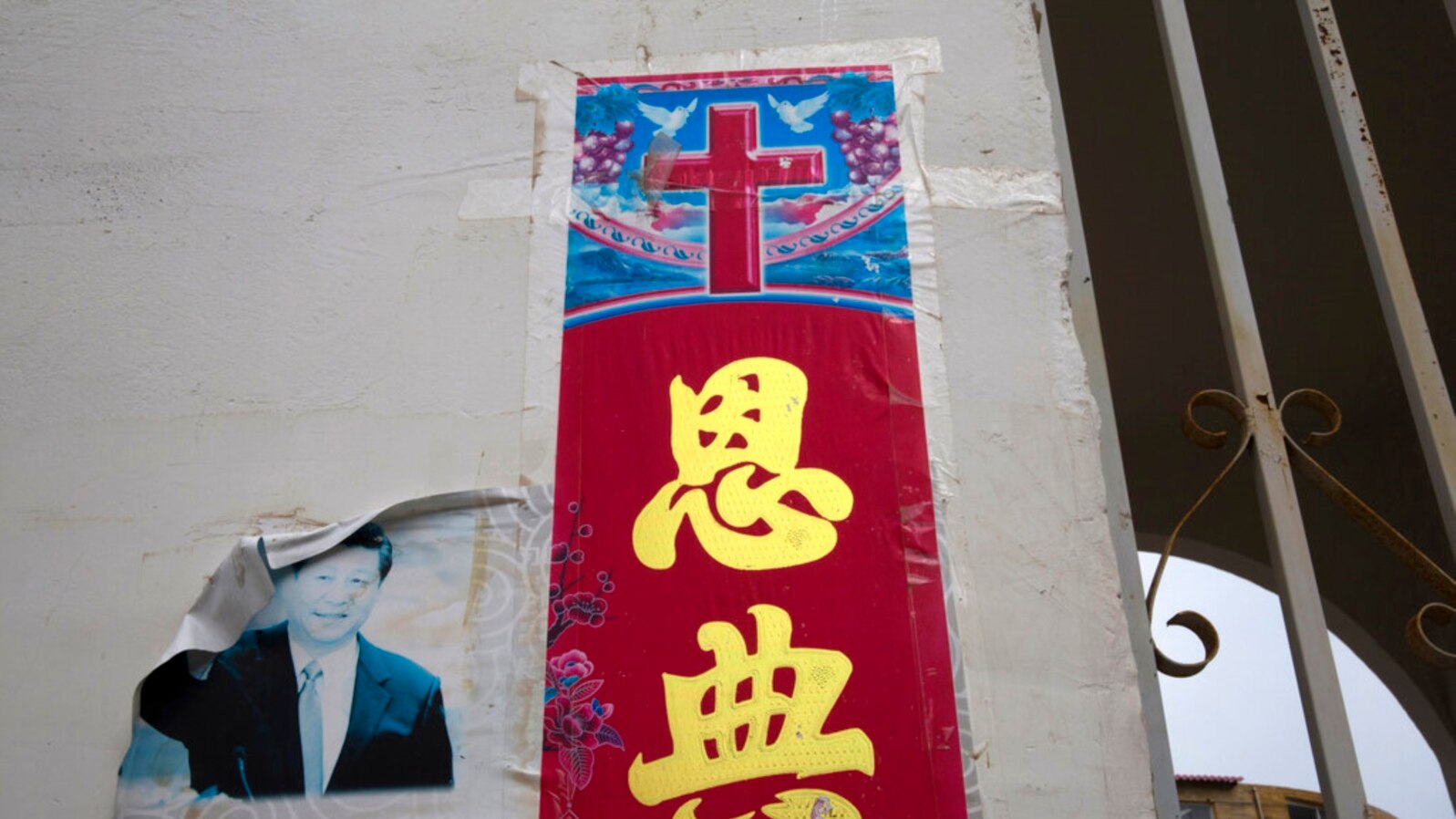 FILE - A faded photo of Chinese President Xi Jinping is posted near a Christian poster with the word "Grace" outside a house church near Nanyang, Henan Province, on June 1, 2018. The Patriotic Education Law, which took effect Jan. 1, 2024, targets religious teaching.