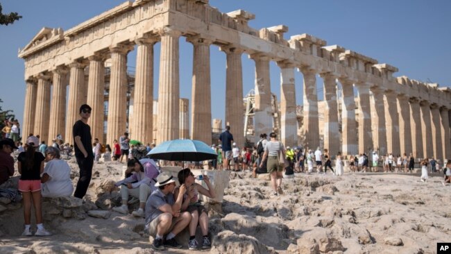 FILE - A tourist drinks water as she and a man sit under an umbrella in front of the Parthenon at the Acropolis during a heat wave in Greece, July 13, 2023.