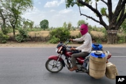 Seorang tukang susu mengendarai sepeda motornya dengan menutup wadahnya dengan karung goni basah untuk mencegah susu rusak akibat panas yang menyengat di Lalitpur, negara bagian Uttar Pradesh, India, Sabtu, 17 Juni 2023. (AP/Rajesh Kumar Singh)