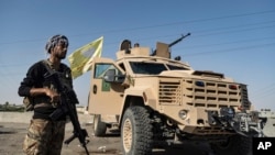 FILE - A U.S.-backed Syrian Democratic Forces fighter stands next to an armored vehicle in the eastern countryside of Deir el-Zour, Syria, Sept. 4, 2023. New attacks between SDF fighters and Iran-backed Syrian government forces were launched in the area Sept. 20, 2024.