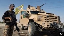 FILE - A U.S.-backed Syrian Democratic Forces fighter stands next to an armored vehicle at al-Sabha town in the eastern countryside of Deir el-Zour, Syria, Sept. 4, 2023.