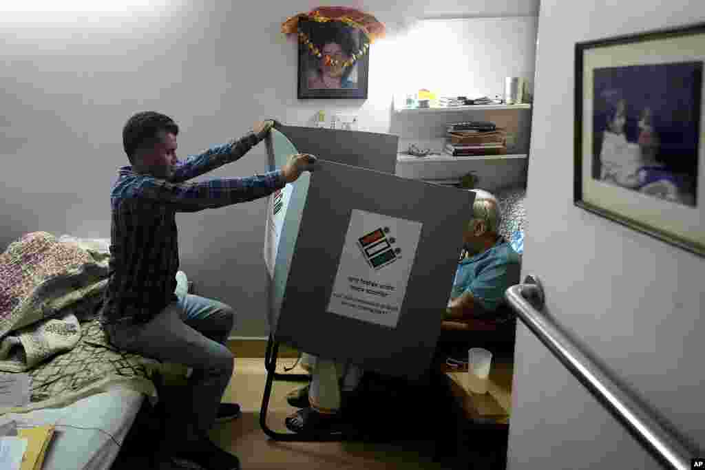 A polling officer holds a voting compartment as an elderly person casts his vote sitting in his home, in New Delhi, India.