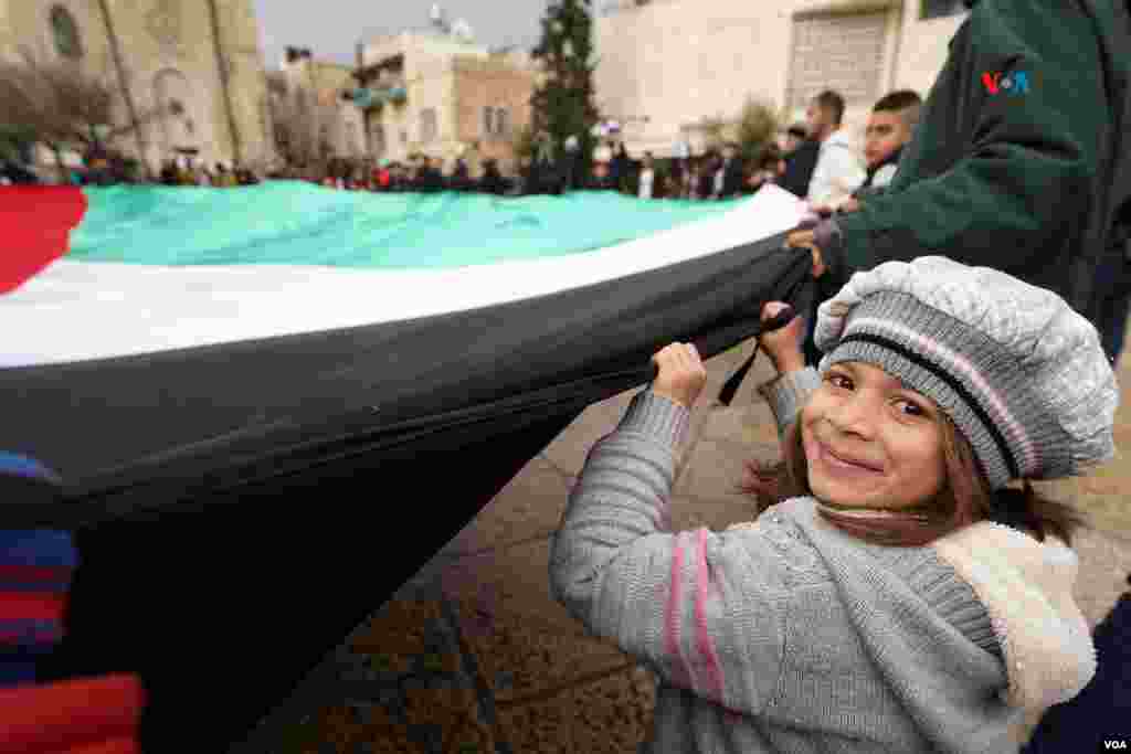 Una niña sostiene, junto a decenas de personas, una bandera gigante de Palestina en la plaza central de la ciudad de Belén, que este año no festejará la Navidad en medio del luto por los miles de fallecidos en Gaza.